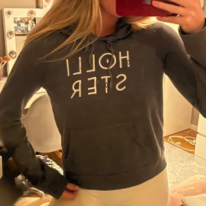 Grå hoodie från Hollister - Säljer en snygg grå hoodie från Hollister i bra skick. Den har en klassisk design med justerbar huva och en stor ficka fram. Perfekt för en avslappnad stil och passar till alla årstider. Texten på framsidan ger en cool touch. Perfekt för vardagsbruk!