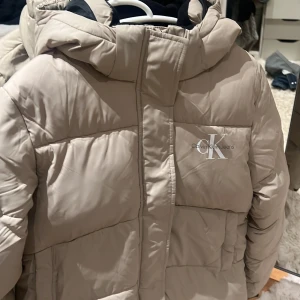 Beige jacka från Calvin Klein Jeans - Säljer en superfin beige pufferjacka från Calvin Klein Jeans. Jackan är i nytt skick och aldrig använd. ( pris lapparna är till och med kvar ). Jättevarmt och snygg🥰Nypris: 2100kr