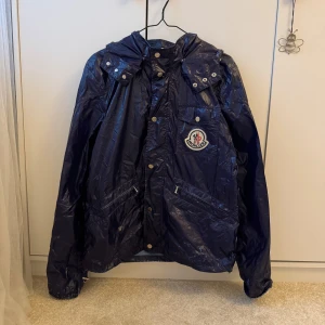 Moncler jacka - Jacka från moncler, mörklila/blå i färgen. I ett tunt fint material som liknar vind-/regnjacka💜 Vintage och har därav ej qr-kod, köpt på Vestiaire och såklart äkta! Storlek 4. Den här små slitningar på nedre delen, se sista bilden