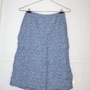 Blommig kjol från Hennes Collection - Säljer en superfin blommig kjol från Hennes Collection i storlek 34. Den är blå med ett sött blommönster och har en dragkedja i bak. Perfekt för vår och sommar! 🌸