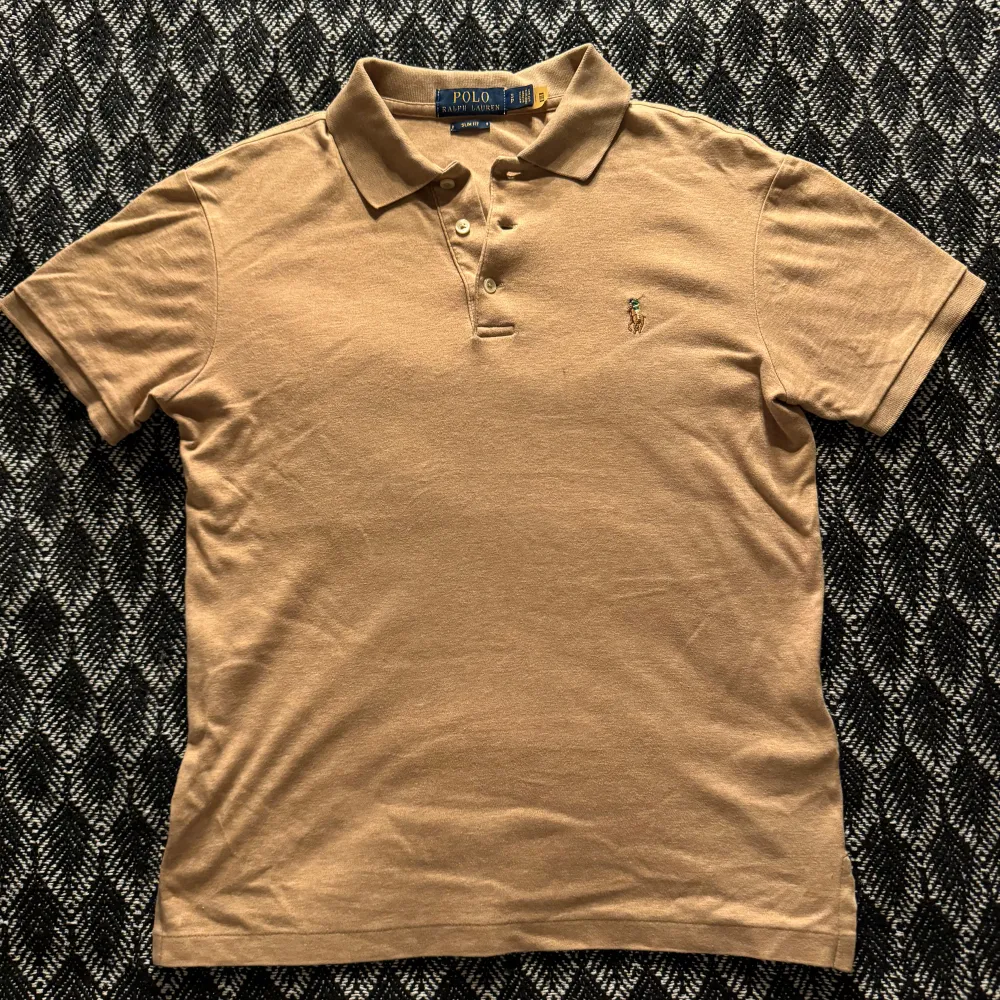 Beige Polo Ralph Lauren pikétröja – Storlek S  Klassisk beige pikétröja från Polo Ralph Lauren i storlek Small. Skjortan är i perfekt skick och är både stilren och tidlös – ett måste i varje garderob. 	•	Skick: Perfekt, nästan som ny 	•	Storlek: S (Small) 	•	Färg: Beige  Perfekt för både vardagsbruk och mer formella tillfällen.. Skjortor.