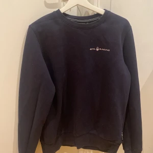 Svart tröja från Sail Racing - Säljer en svart tröja från Sail Racing i bra skick. Den har en enkel design med logotypen på bröstet och en liten detalj på ryggen. Perfekt för höst och vinter med sin bekväma passform och långa ärmar. Passar både till vardags och mer avslappnade tillfällen.
