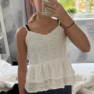 Vit blommig topp med volang - Säljer en superfin vit topp med blommigt mönster och volangdetaljer. Den har smala axelband och en dragkedja på sidan för enkel påklädning. Perfekt för sommardagar eller en avslappnad vårlook. Toppen är i mycket bra skick och passar perfekt till jeans eller kjol. Jag köpte den för cirka 150 kr så jag säljer den för väldigt bra pris. 