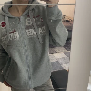 Grå hoodie med dragkedja - Säljer en grå hoodie med dragkedja och tryck på bröstet. Den är använd ett par gånger men är i väldigt bra skick. Den är jättefin och oversize på mig.