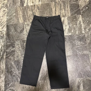 Svarta byxor från Uniqlos U kollektion - Säljer ett par c00la byxor från Uniqlos U kollektion. Med den respekterade designern Christophe Lemaire i spetsen. Byxorna är i bra skick. De är tillverkade i en bomullstwill som påminner om ett par mjuka chinos. Perfekta för både vardag och mer formella tillfällen. Midjan är 33 tum och de har en wide tapered passform.        Hör av er vid frågor!🫡🫡 