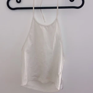 Vit satinlinne - Säljer ett stilrent vitt linne i material. Perfekt för sommardagar eller som ett basplagg under en kavaj. Linnet har en enkel design med smala axelband och en mjuk, glansig yta. Passar både till vardags och festliga tillfällen.