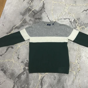 Grå och grön tröja från GANT - Säljer en snygg och stilren tröja från GANT i storlek M. Den har en grå överdel, vit mitt och mörkgrön nederdel. Perfekt för både höst och vinter med sin mjuka och varma känsla. Tröjan har långa ärmar och en klassisk rund halsringning.