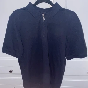 Svart pikétröja från Jack & Jones - Säljer en stilren svart pikétröja från Jack & Jones. Den har en dragkedja framtill och korta ärmar, perfekt för både vardag och fest. Tröjan är i bra skick och passar till många olika outfits. Perfekt för dig som gillar en klassisk look!