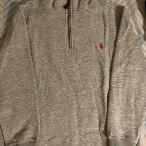 Grå hoodie från Polo Ralph Lauren - Säljer en snygg grå hoodie från Polo Ralph Lauren i storlek S. Den har en halv dragkedja och det klassiska röda broderade logotypen på bröstet. Perfekt för en avslappnad stil och passar till alla årstider. Superbekväm och i bra skick!