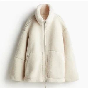 Vit teddyjacka med dragkedja - Mysig vit teddyjacka perfekt för kyliga dagar. Den har en dragkedja framtill och stora fickor för extra värme och stil. Jackan är långärmad och har en hög krage som skyddar mot vinden. Perfekt för höst och vinter!