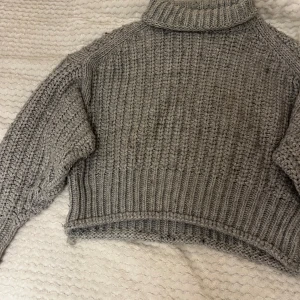 Grå stickad polotröja - Säljer en supermysig grå stickad polotröja. Perfekt för kyliga dagar med sin croppade design och långa ärmar. Den har en ribbad struktur som ger en snygg look. Ett måste i garderoben för höst och vinter!