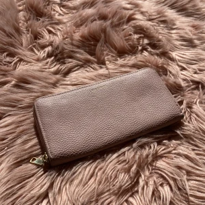 Beige plånbok med dragkedja - Säljer en stilren och praktisk beige plånbok i skinn. Den har en dragkedja runtom och flera fack inuti för kort och mynt. Perfekt för att hålla ordning på dina saker med stil!