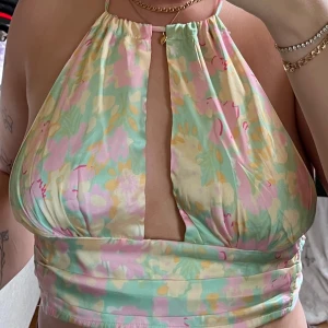 Färgglad halterneck topp - Säljer en superfin halterneck topp med ett färgglatt mönster i pastellfärger som rosa, grön och gul. Toppen har en snygg öppen rygg och knyts i nacken och bak. Perfekt för sommarens fester eller en dag på stranden!