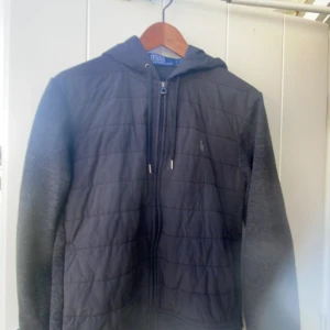 Svart jacka från Polo Ralph Lauren - Säljer en snygg svart cardigan från Polo Ralph Lauren. Den har en quiltad design på framsidan och är utrustad med en dragkedja. Den har en huva och långa ärmar, perfekt för höst och vår. Den är i bra skick! Det är en size S. Jag är 175cm och den sitter lite tajt vid midjan men annars luftig på överkroppen och armarna