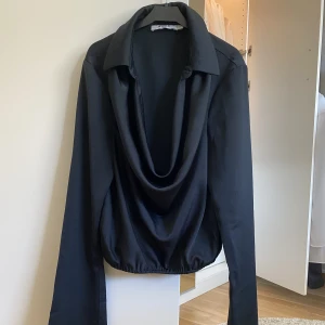 Blus - Svart siden blus med u ringning. Den är Kroppad nedtill med vida ärmar