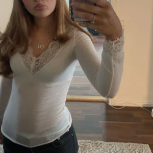 Vit intimissimi tröja med spetsdetaljer - Söt vit långärmad topp med v-ringad spetsdetalj vid hals och ärmslut. Perfekt för en stilren look. I färgen vanilj💗