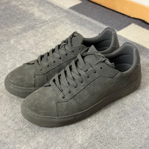 Grå grisch sneakers med snörning - Snygga grå sneakers i mocka med diskret perforerat mönster på sidan. Skorna har en klassisk design med snörning och en bekväm sula. Perfekta för en stilren look.