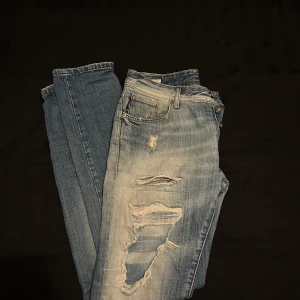 Jack & Jones LmtEd - Säljer ett par blå jeans med slitningar och knappgylf. De har en klassisk femficksdesign och en ljus tvätt som ger en avslappnad look. Perfekta för en casual stil. Kontakta oss vid frågor och funderingar 