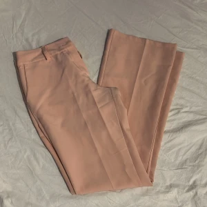 Rosa kostymbyxor från Design by Si - Snygga rosa lågmidjade kostymbyxor från Design by Si. De har en klassisk design med raka ben och en knapp i midjan. Perfekta för en stilren look.