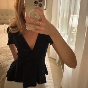 Mörkblå omlottopp - Snygg mörkblå omlottopp med korta ärmar och volangdetaljer i midjan. Perfekt för en stilren look.