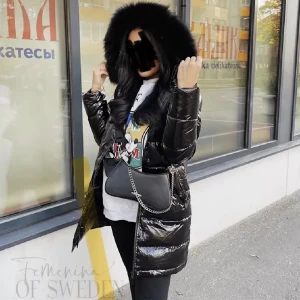 Svart glansig dunjacka med pälsdetaljer - Snygg svart glansig dunjacka från Feminine of Sweden med stor huva och pälsdetaljer. Jackan har en lång design och dragkedja framtill. Perfekt för kyliga dagar när du vill hålla stilen.