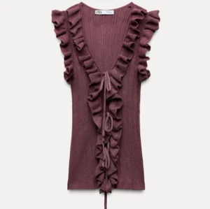 Populära vinröd volangtopp från Zara - Säljer en vinröd ribbad topp från Zara med volangdetaljer längs den djupa v-ringningen. Toppen är ärmlös och har knytband framtill för en justerbar passform. Perfekt för en trendig look! Ny med prislapp på!