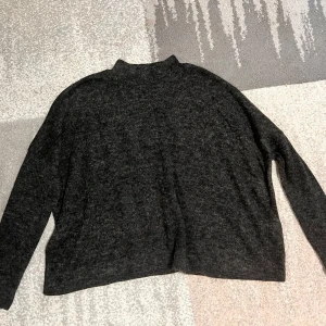 Mörkgrå stickad tröja - Säljer en mysig mörkgrå stickad tröja med hög krage. Tröjan har en lös passform och långa ärmar, perfekt för kyliga dagar. 