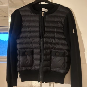 Svart jacka från Moncler - Svart cardigan från Moncler i storlek 2, vilket passar XS/S. Den ena sidan på etiketten har lossnat (andra bilden) men inget som syns och annars i bra skick. Skriv privat om ni vill ha fler bilder eller information.