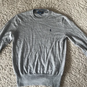 Ralph Lauren tröja - Säljer en stilren grå tröja från Ralph Lauren med rund hals och broderad logga på bröstet. Tröjan har långa ärmar och ribbade muddar vid ärmslut och nederkant. Perfekt för en avslappnad men snygg look. Tröjan är storlek 14-16 år i barnstorlek. 