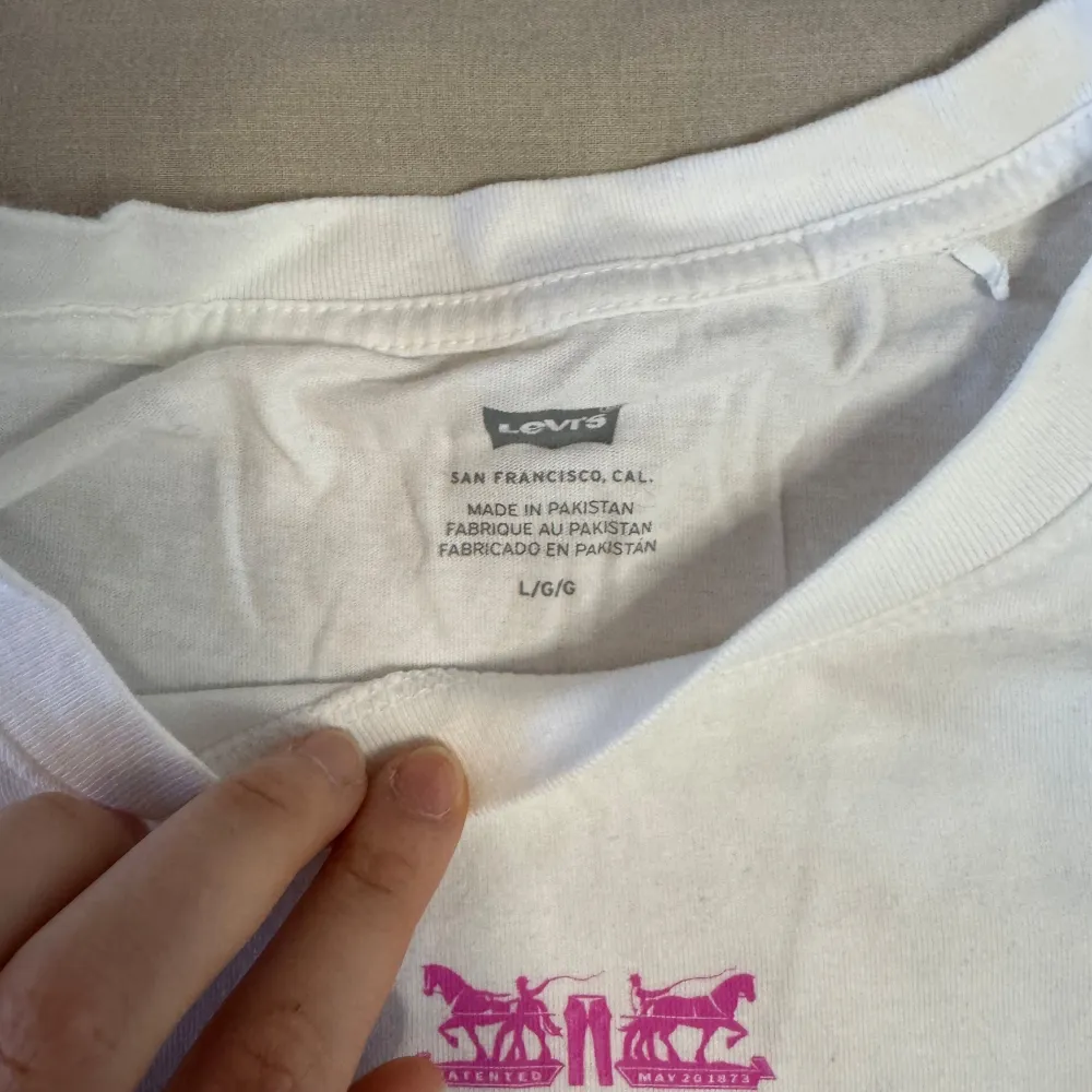 Säljer en vit t-shirt från Levi's med färgglatt broderat 'Levi Strauss & Co.' på bröstet. T-shirten har en klassisk rund hals och korta ärmar. Perfekt för en avslappnad stil. T-shirten är aldrig använd, men saknar etticket. Storlek L. T-paidat.