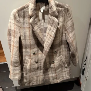Rutig kavaj - Snygg rutig kavaj i beige och grå toner med dubbelknäppning och klassisk krage. Endast använd ett fåtal gånger. Den har långa ärmar och två fickor framtill. Perfekt för en stilren look.
