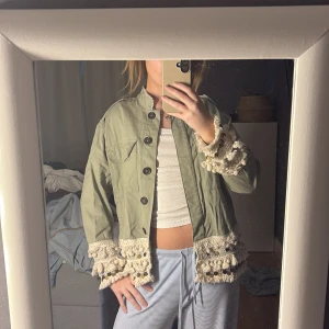 Grön jacka med spetsdetaljer - Säljer en unik grön jacka med vackra spetsdetaljer vid ärmslut och nederkant. Jackan har knappar framtill och en avslappnad passform. Perfekt för att ge din outfit en bohemisk touch. storlek M men passar mig som är xs/s