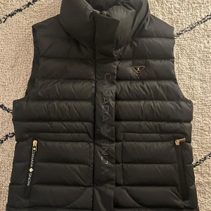 Grön dunväst från Canada Snow - Mörkgrön dunväst från Canada Snow, Lea  med hög krage och dragkedja. Västen har två fickor med dragkedjor och en stilren design. Perfekt för kyliga dagar. Storlek M. Knappt använd och är som ny. Inköpt för 1800kr. Säljes för 800kr.