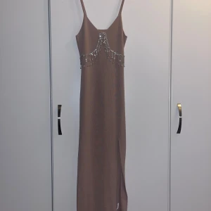 Beige klänning - Elegant beige långklänning med smala axelband och dekorativa pärlor framtill. Klänningen har en slits på sidan som ger en stilfull touch. Perfekt för speciella tillfällen. Köpt i Stockholm, använd en gång! Finns små defekter men väldigt osynliga! ✨