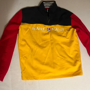 Flerfärgad tröja från Karl Kani - Säljer en cool flerfärgad tröja från Karl Kani. Tröjan har en gul kropp, röda ärmar och mörkblått axelparti med dragkedja vid halsen.