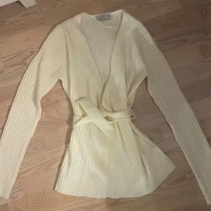 Gul ribbad kofta från MANGO - Säljer en stilren gul ribbad kofta från MANGO. Koftan har långa ärmar och ett knytbälte i midjan för en elegant passform. Perfekt för att lägga till en touch av färg till din garderob. 🌼