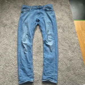Blå jeans från Tiger of Sweden - Snygga blå jeans från Tiger of Sweden med klassisk femficksdesign och knappgylf. Perfekta för en stilren look. Märkesdetaljer syns på fickan och bak i midjan.