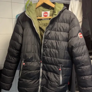 Svart pufferjacka från Colmar - Snygg svart pufferjacka från Colmar med en grön insida och huva. Jackan har en dragkedja framtill och två fickor med dragkedjor. Perfekt nu till våren då den är lite tunnare. Passar perfekt på mig som är 185 men köpte när jag va 180 så märker ingen skillnad. Priset är inte hugget i sten så kom med bud jag tar första bästa pris
