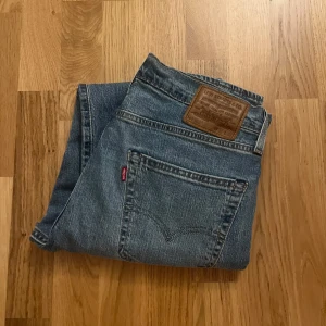Blå jeans från Levi's 502 - Säljer ett par klassiska blå Levi's jeans med rak passform. De har en traditionell femficksdesign och en läderpatch med logotyp på baksidan. Perfekta för en avslappnad stil.                                     Storlek:                                                                              W:32 L:32