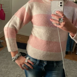 Rosa och vit randig stickad tröja - Säljer en mysig stickad tröja med breda ränder i rosa och vitt. Tröjan har långa ärmar och en rund halsringning. Perfekt för kyligare dagar!