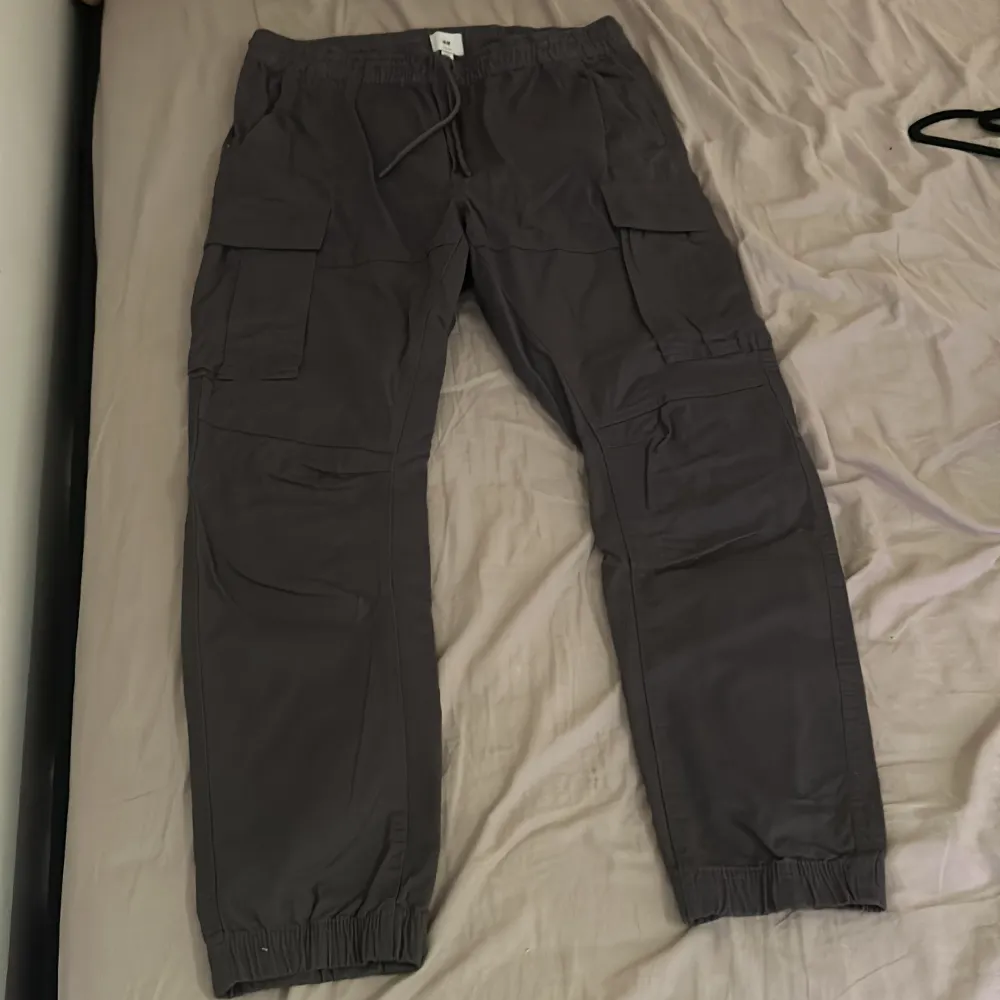 Snygga grå cargobyxor från H&M i slim fit. Byxorna har elastisk midja med snörning och flera praktiska fickor på sidorna. Perfekta för en avslappnad stil.. Farkut & Housut.