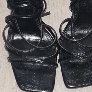 Svarta sandaler med snörning - Snygga svarta sandaler från Zara med elegant snörning. Perfekta för en stilren look. Sandalerna har en fyrkantig tå och är tillverkade i syntetmaterial.