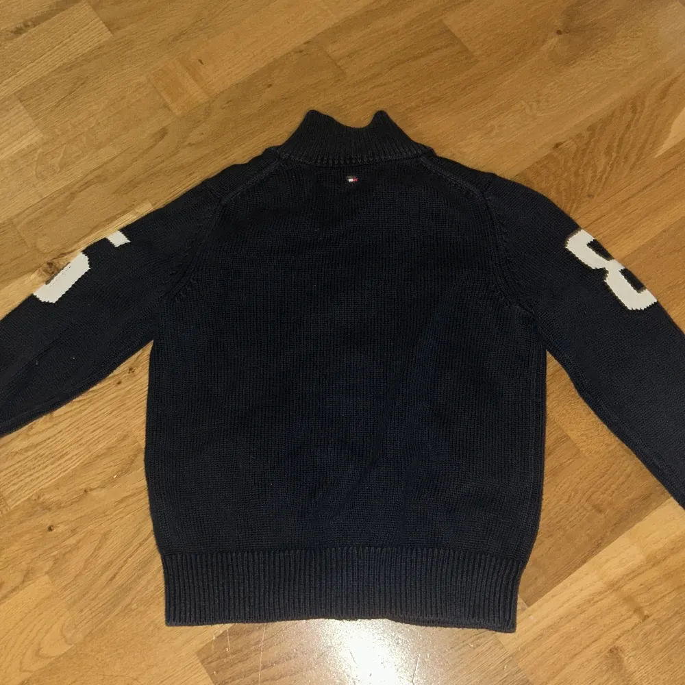 Säljer en snygg mörkblå stickad kofta från Tommy Hilfiger med dragkedja och ribbade detaljer. Koftan har långa ärmar med vita siffror på ärmarna och en liten logga på bröstet. Perfekt för en stilren look! Säljer då den är för små barn och den inte kommer till anvönda för någon i familjen. Neuletakit & Villapaidat.