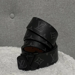 Lv bälte svart - Snyggt svart bälte från Louis Vuitton med det klassiska LV-mönstret och en stilren svart spänne. Tillverkat i Frankrike, detta bälte är perfekt för att ge en lyxig touch till din outfit. 125cm vid frågor eller funderingar hör av er!