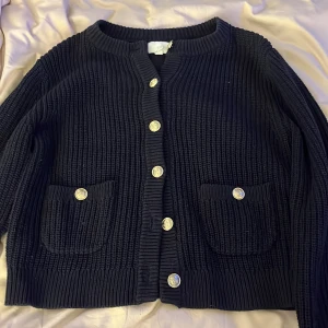 Marinblå stickad kofta från H&M - Säljer en svart stickad kofta från H&M med snygga knappar framtill och två praktiska fickor. Perfekt för kyliga dagar och enkel att matcha med olika outfits. 🖤