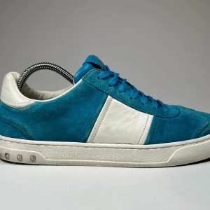 Blå och vita sneakers från Valentino - Snygga blå sneakers i mocka med vita detaljer från Valentino. Skorna har en klassisk design med snörning och en vit sula. Perfekta för en stilren look.