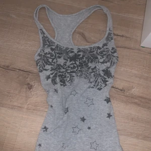 Grå ribbad linnetopp med stjärnmönster - Snygg grå ribbad linnetopp med ett coolt stjärnmönster i svart. Perfekt för en avslappnad stil. Toppen har en tight passform och ärmlös design.