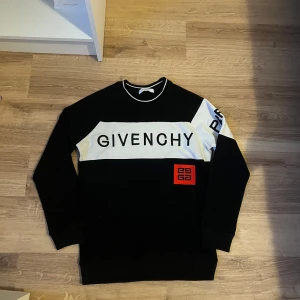 Svart/vit tröja från Givenchy - Snygg svart och vit tröja från Givenchy med stor logotyp på bröstet och en röd detalj. Tröjan har långa ärmar och en klassisk passform. Perfekt för en stilren look.