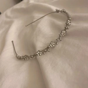 Silverfärgad diadem med blommor - Ett elegant diadem i silverfärg med glittrande blommor. Perfekt för speciella tillfällen som bal eller fest. Blommorna är utsmyckade med små stenar som ger en extra touch av glamour. Passar bra till både uppsatt och utsläppt hår. Använd en gång