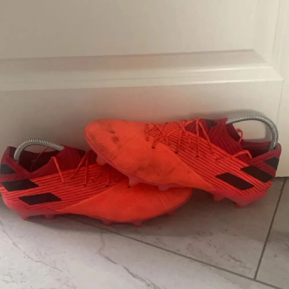 Säljer ett par röda Adidas Nemeziz fotbollsskor. De har en cool design med svarta detaljer och snörning. Skorna är i välanvänt skick men fortfarande grymma för spel på planen. Perfekta för dig som älskar att dominera matchen!. Skor.